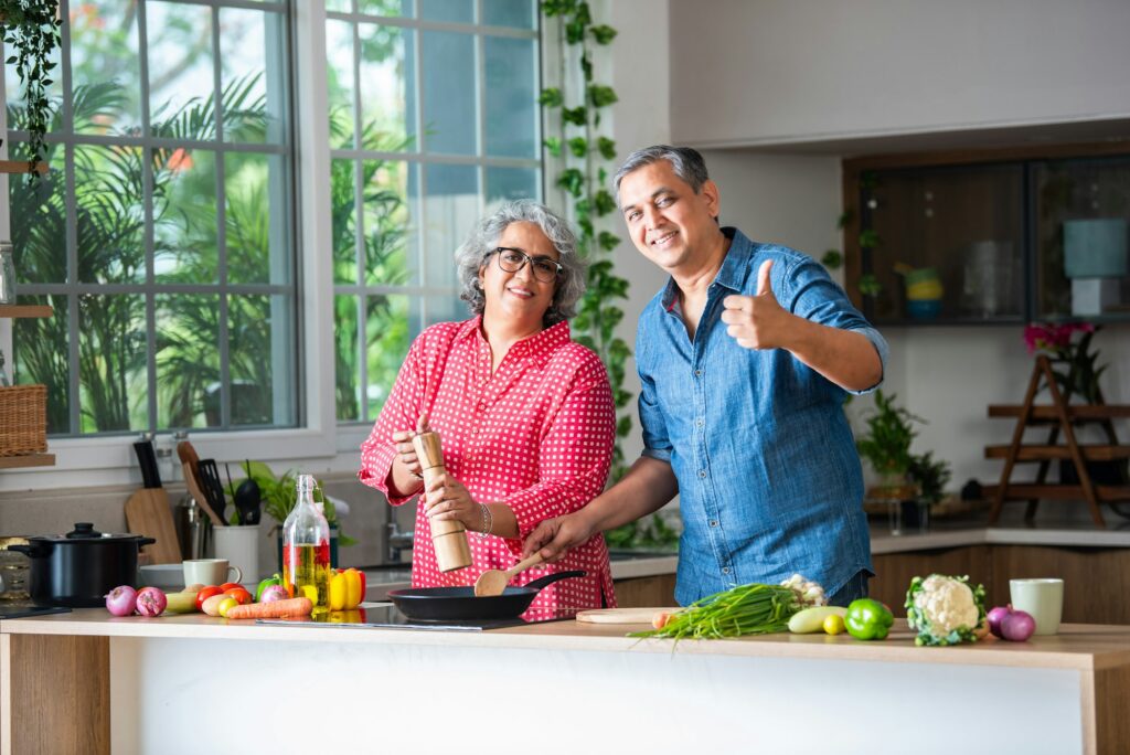 Senior Indian asian couple in kitchen, cooking food together and happy in retirement lifestyle